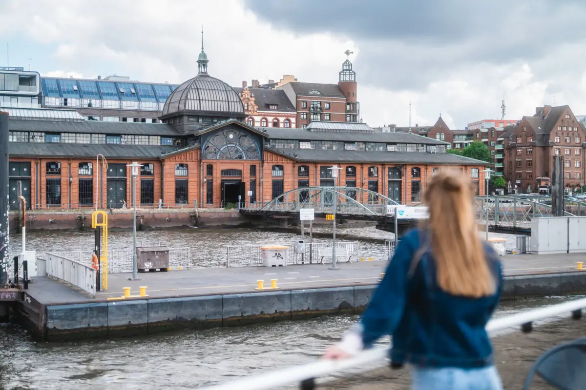Eine Frau steht auf einem Schiff und blickt auf ein Gebäude.