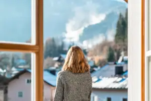 Eine Frau blickt aus einem Fenster auf eine Bergkette.