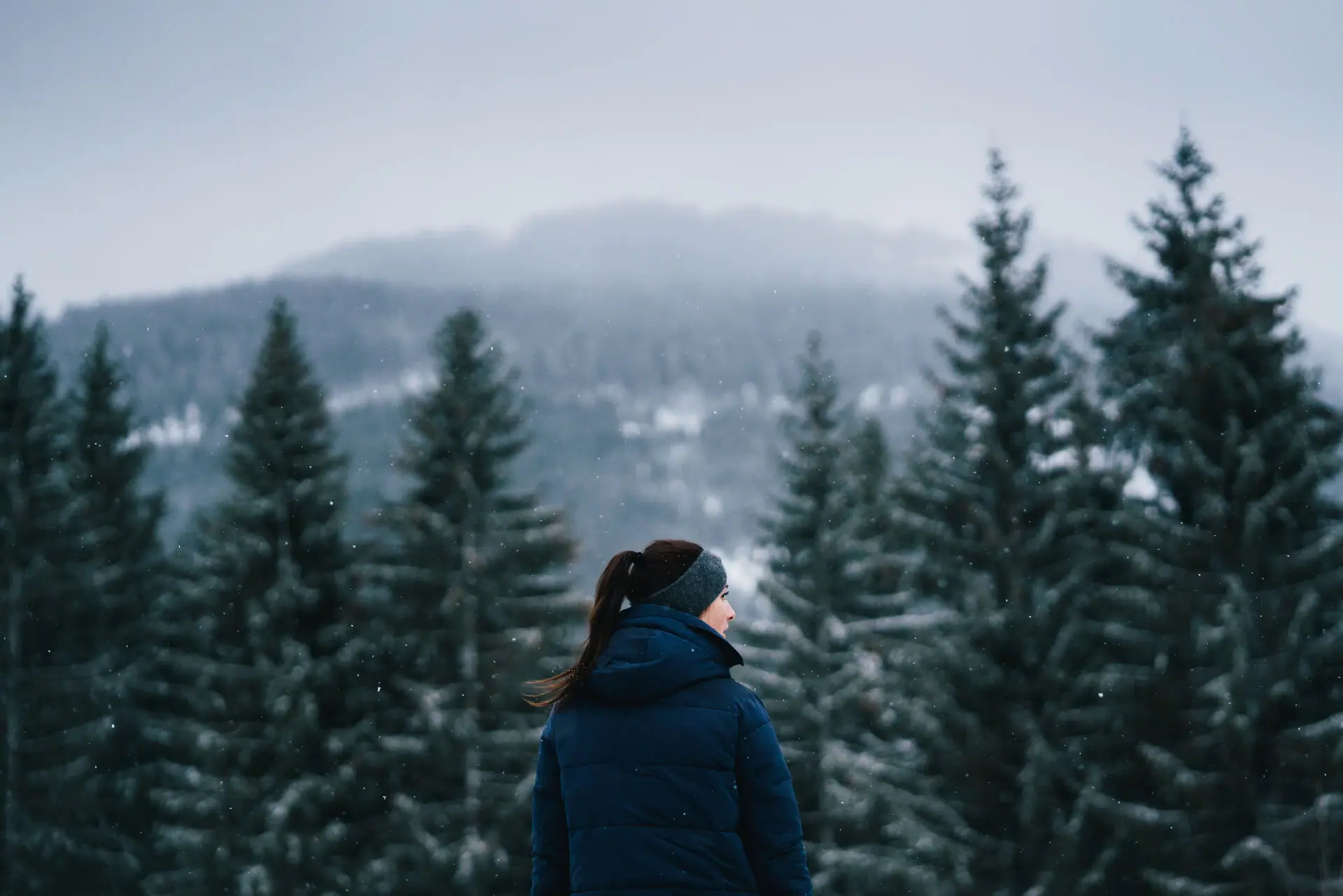 Eine Frau steht vor schneebedeckten Bäumen im Freien.