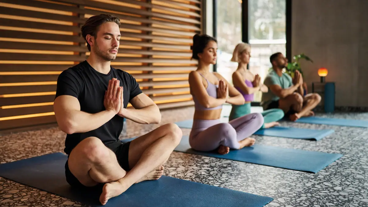 Eine Gruppe von Menschen sitzt auf Yogamatten mit zusammengelegten Händen.