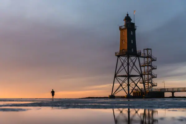 Eine Person geht am Strand neben dem Leuchtturm Obereversand entlang.