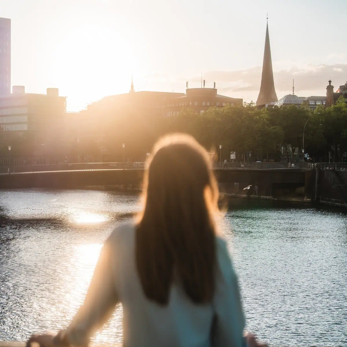 Eine Frau steht auf einer Brücke und blickt auf eine Stadt.