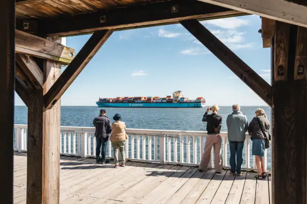 Eine Gruppe von Menschen betrachtet ein großes Schiff auf der Aussichtsplattform Alte Liebe in Cuxhaven.
