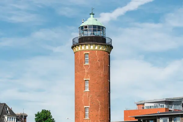 Der Hamburger Leuchtturm in Cuxhaven mit grünem Dach und einem Gebäude im Hintergrund.